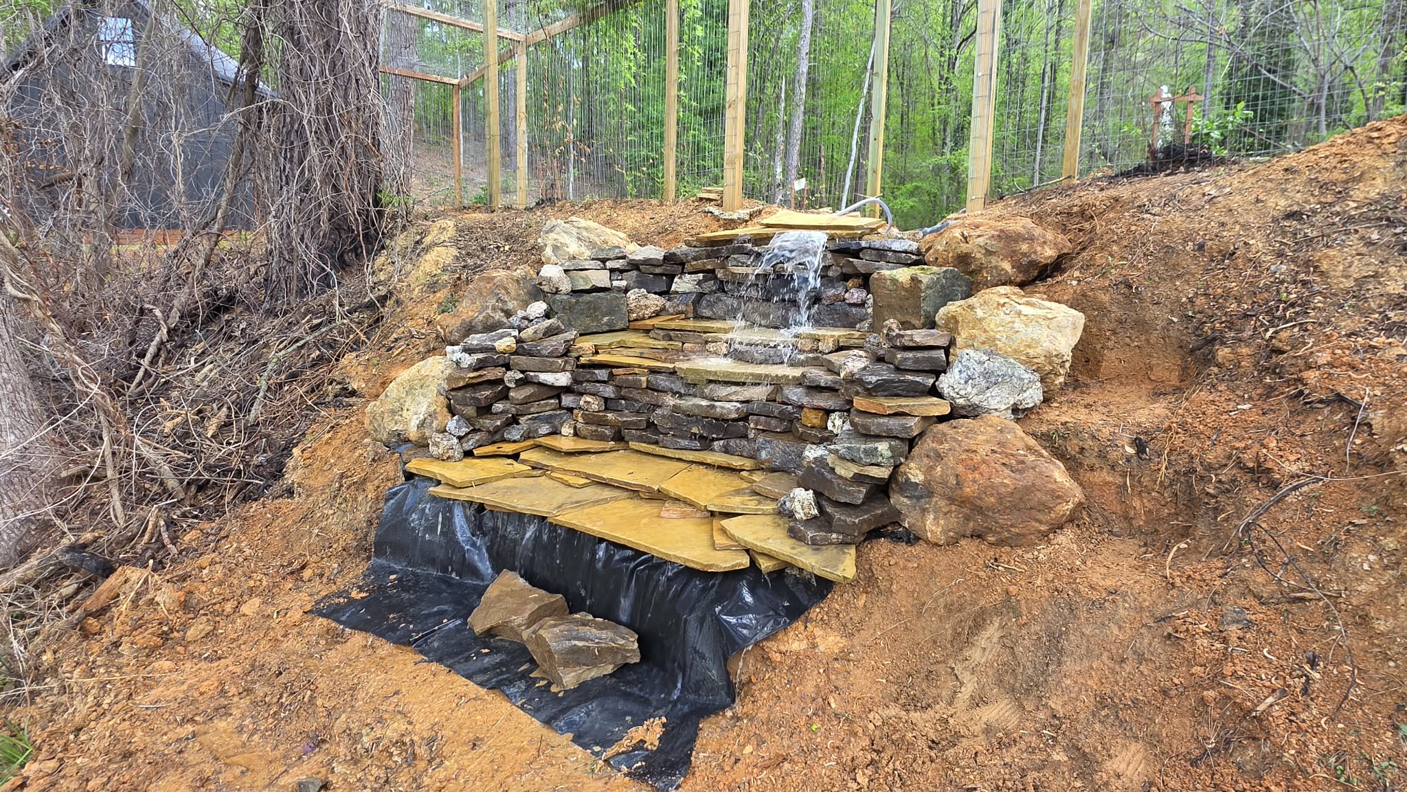 Chris hand-stacking the stone waterfall inside the vining pergola — in progress 2025